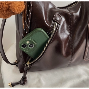 Detail of dark brown glossy leather shoulder bag showing side zipper pocket and storage depth