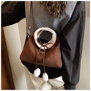Détail du sac bandoulière en daim marron avec anse en fausse fourrure blanche et pompon