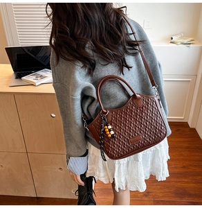 Close-up of brown woven bucket bag featuring rounded handles and a colorful bead charm