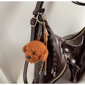 Detail of cute brown teddy dog plush pendant with woven ropes on a leather shoulder bag