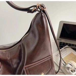 Detail of dark brown leather shoulder bag with gold buckle side pocket and glossy finish