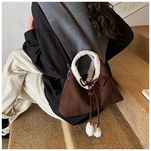 Détail d'un sac à main marron en daim avec poignées en peluche blanche et pompons