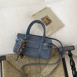 Detail of navy blue suede crossbody bag on woven chair with golden key ornament