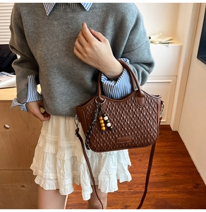 Detail of dark brown woven texture bucket bag with wooden bead charm and long shoulder strap
