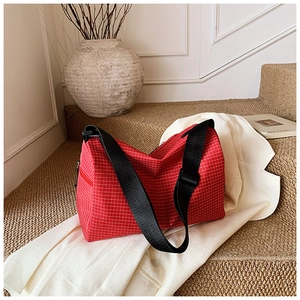 Detail of red plaid crossbody bag with black nylon strap and textured canvas surface