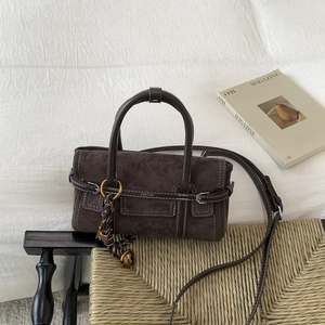 Detail of dark coffee suede crossbody bag featuring stitch lines and vintage bell charm