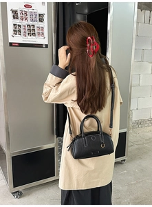 Close-up of black pebbled leather Boston bag with contrast white stitching and metal ring detail