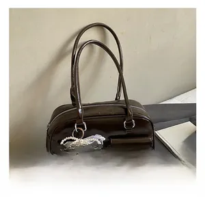 Detail of dark coffee patent leather handbag with a pearl bow charm and front pocket