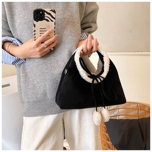 Détail du sac en daim noir avec bordure en similicuir et pompons en fourrure