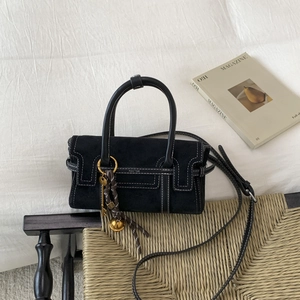 Detail of black suede handbag with contrast white stitching and metal key charm