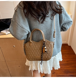 Detail of a brown embossed bucket bag with woven texture and bohemian beaded charm