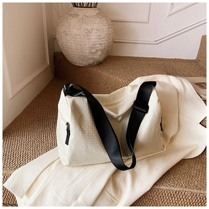 Detailed view of cream-colored textured duffel bag on a trench coat background