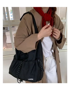 Detailed close-up of a large black drawstring crossbody bag with fashion label decoration