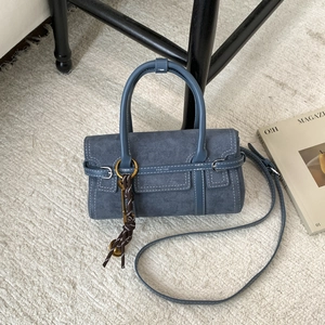 Detail of blue suede crossbody bag with stitching and decorative woven pendant