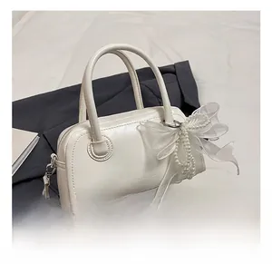 Détail du sac polochon en similicuir blanc avec nœud en organza et chaîne perlée