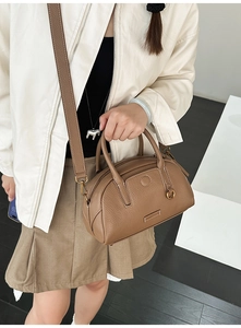 Detailed side view of a brown pebbled leather bowling bag with gold hardware and strap