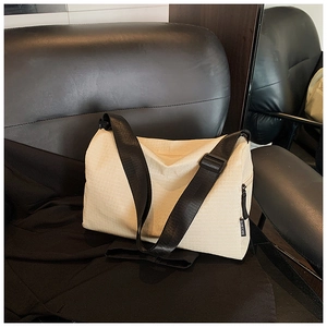 Detailed view of cream canvas crossbody bag with wide black strap and side label detail