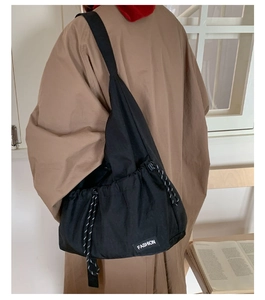 Detail of black drawstring crossbody bag with fashion label and wide shoulder strap