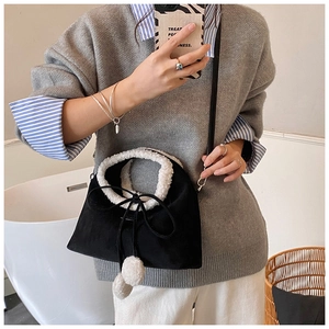Détail du sac bandoulière en suédine noire avec poignées en sherpa et pompons décoratifs