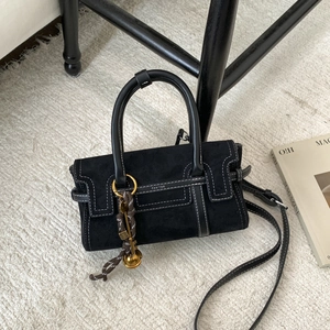 Detail of a black suede handbag with white contrast stitching and a gold charm