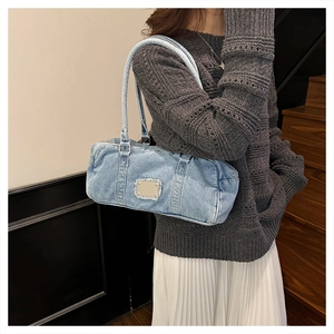 Detail of washed denim shoulder bag with silver metal plaque and frayed edges texture