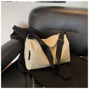 Detail of the cream textured messenger bag featuring a wide black strap and urban style