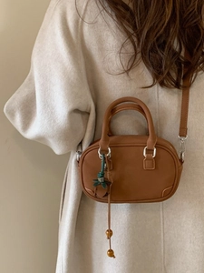 Brown mini oval crossbody bag with strawberry charm shown on a model's back