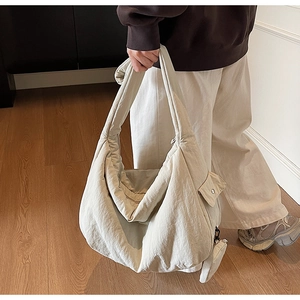 Detail einer großen cremefarbenen Stepptasche mit passendem Gurt und kleinem Anhänger