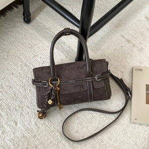 Detail of dark brown suede handbag with white contrast stitching and gold key charm