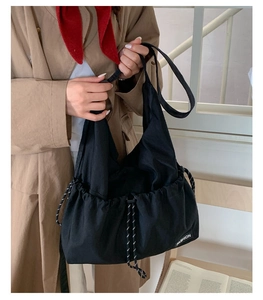 Detail of black canvas drawstring bag featuring white fashion label on khaki trench coat