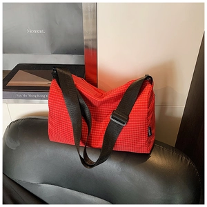 Detail of red plaid pattern shoulder bag with adjustable strap on leather seat