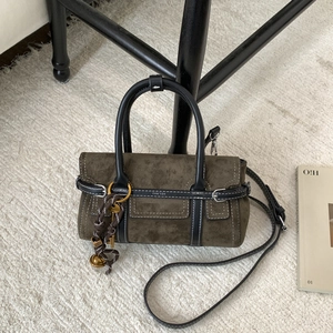 Detail of olive suede crossbody bag with contrast stitching and decorative braided knot