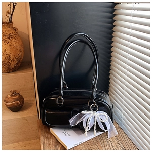 Detail view of black glossy shoulder bag featuring a white organza bow and pearl charm