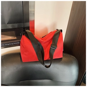 Detail of red checkered crossbody bag with adjustable black strap on black leather sofa