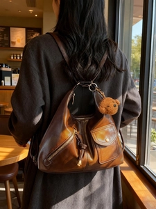 Retro brown leather shoulder bag with plush bear charm worn in a cozy cafe setting