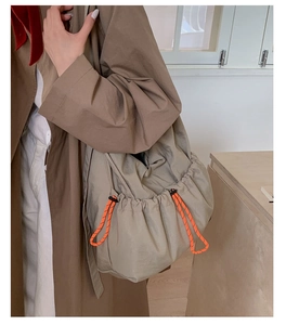 Side view of large nylon drawstring crossbody bag in khaki with orange accent cord