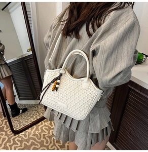 Detailed shot of white woven texture bucket bag with beaded tassel charm on a model