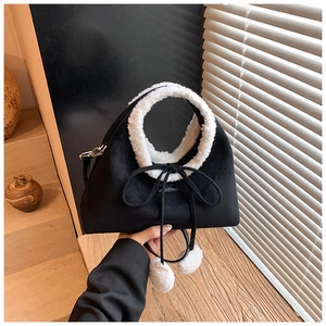 Détail d'un sac en daim noir avec bordure en polaire blanche et pompon décoratif doux