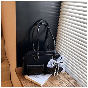 Detail of a black canvas underarm bag featuring front double pockets and a lace bow charm