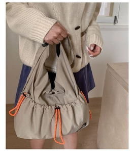Detailed close-up of khaki nylon hobo bag with vibrant orange drawstring accents