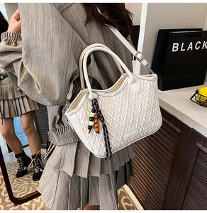 Detailed view of a white quilted bucket bag featuring a wooden bead charm and long strap