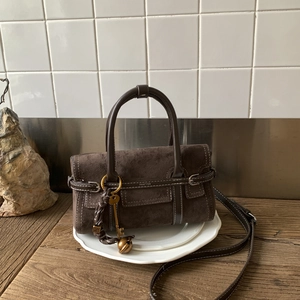 Detail of vintage brown suede crossbody bag with white stitching and metal key charm