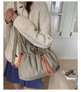 Close-up of khaki drawstring crossbody bag with orange cord and FASHION label