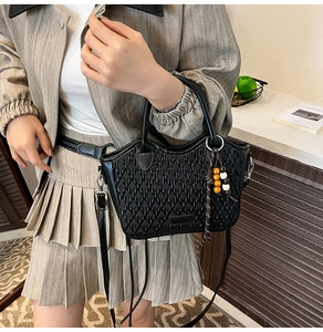 Detail of black woven bucket bag with elegant wooden bead charm and round top handle