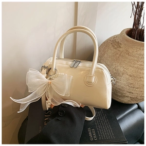 Détail d'un sac Boston crème avec un nœud en organza et un pendentif en perles
