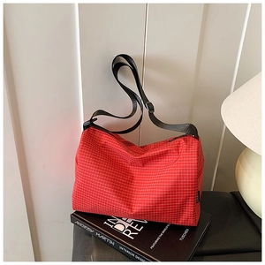 Detail of red checkered crossbody bag with adjustable black strap on a design book