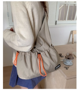 Close-up of beige nylon slouchy bag with orange drawstring details and fashion label