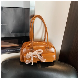 Detail of caramel glossy leather shoulder bag with decorative bows and pearl charms