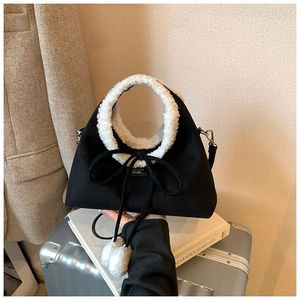 Détail du sac bandoulière en suédine et fausse fourrure avec pompons sur une valise