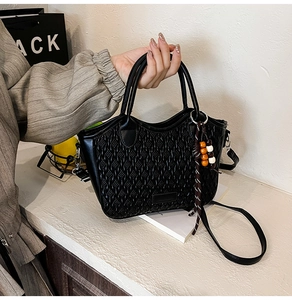 Close-up of black woven texture handbag with decorative beaded charm and shoulder strap